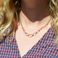 A Caucasian model is wearing the necklace, and the centre hangs slightly below her clavicle. She's wearing a v-neck red and blue gingham blouse.