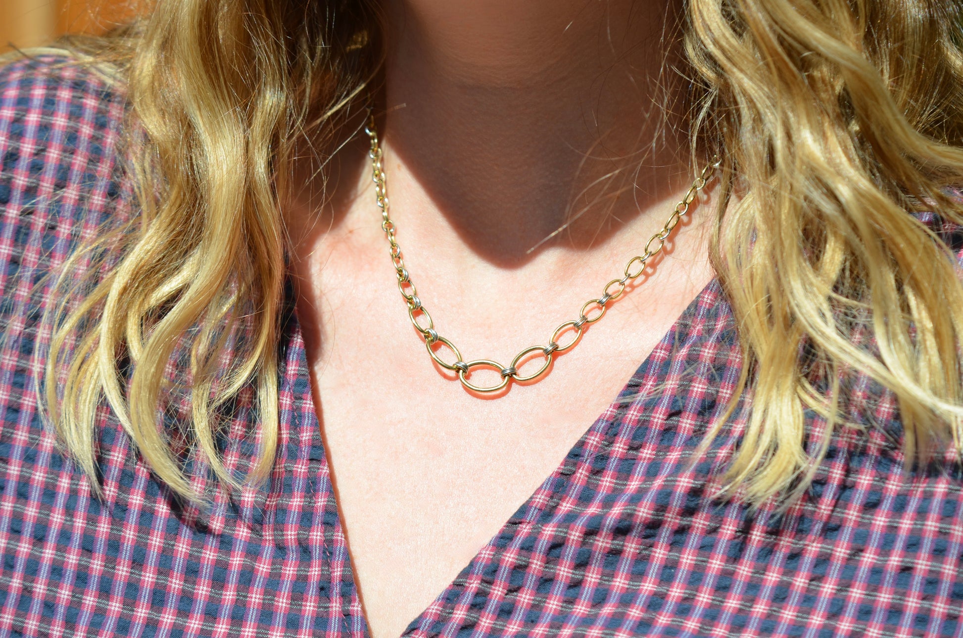 A Caucasian model is wearing the necklace, and the centre hangs slightly below her clavicle. She's wearing a v-neck red and blue gingham blouse.