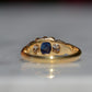 A Victorian ring in yellow gold with swirling shoulders and a central vivid blue sapphire flanked by a pair of old mine cut diamonds, photographed from behind, focused on the back of the mount and rear of the gemstones.