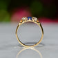 A Victorian ring in yellow gold with swirling shoulders and a central vivid blue sapphire flanked by a pair of old mine cut diamonds, photographed positioned upright looking through the finger hole to showcase the gallery detail and rise off the finger.