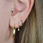 the featured hoops are shown on a caucasian model's first lobe piercing. also visible are a snug gold hoop with dangling diamond in the second piercing, a snug gold hoop stylized as bamboo in the third piercing, and a snug gold hoop stylized as a snake with diamond eyes in the tragus piercing.