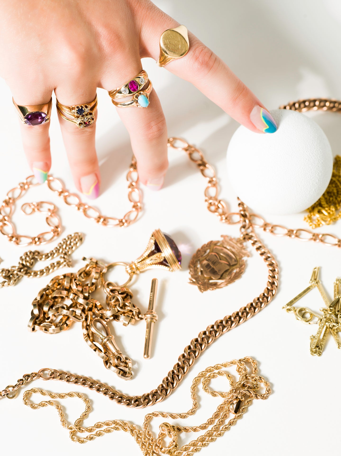 a hand decked out in gold rings and with bright nail art rests among a splayed pile of antique gold chains