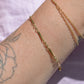 A closely cropped view of the bracelet on a Caucasian model's wrist. She is wearing several other gold bracelets and has a floral tattoo on her forearm.