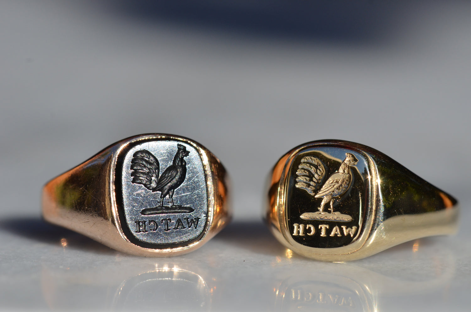 side by side are an original vintage signet ring with carved onyx and the new solid gold double made from its mold: both feature an intaglio of a cockerel and the word WATCH