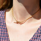 A Caucasian model wears the chain as a necklace, where it fits snugly at the base of her neck in a choker length. She is wearing a v-neck blue and red gingham blouse.