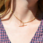 A Caucasian model wears the chain as a necklace, where it fits snugly at the base of her neck in a choker length. She is wearing a v-neck blue and red gingham blouse.