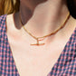 A Caucasian model wears the chain as a necklace, where it fits snugly at the base of her neck in a choker length. She is wearing a v-neck blue and red gingham blouse.