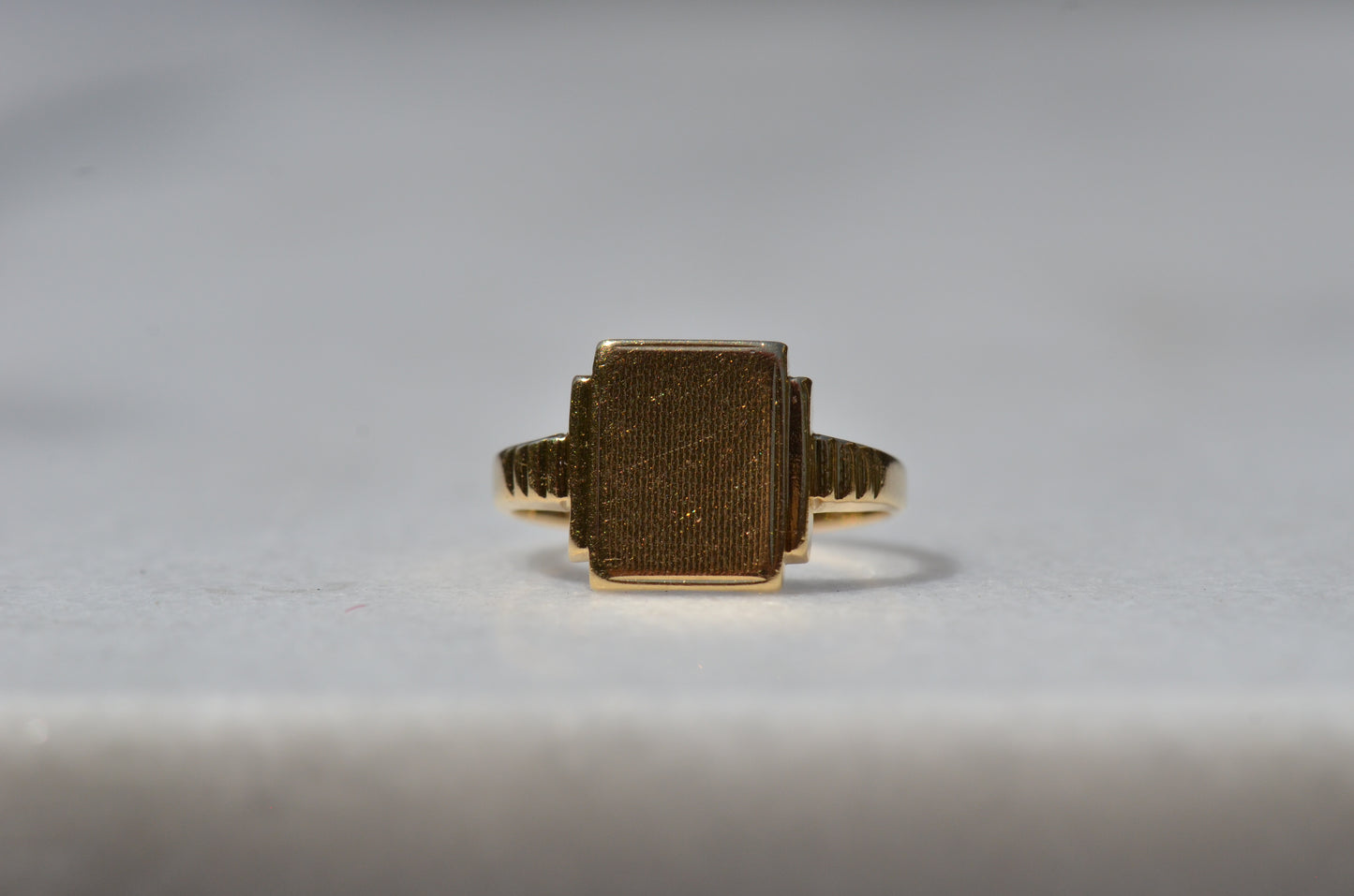 In diffused natural light, the wavy texture of the face of the signet is visible as well as light scratches and scuffs from nearly a century of wear. The ring is viewed head-on.