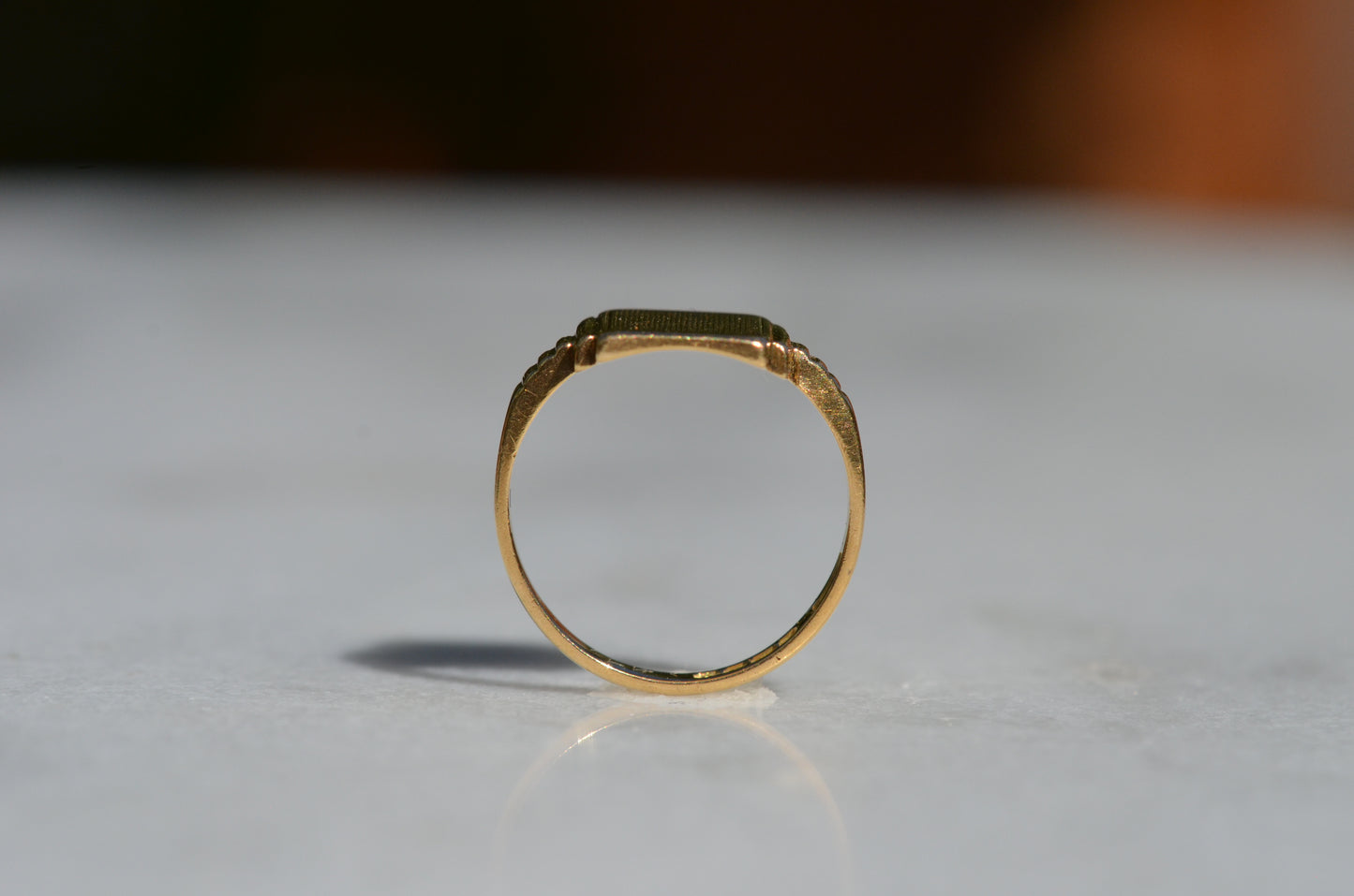 The ring is positioned upright, looking through the finger hole, to show the very low rise of the flat top and the thickness of the notched shoulders.
