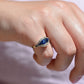 A closely cropped macro of the ring, vibrant in bright daylight, on the right pinky finger of a Caucasian model.