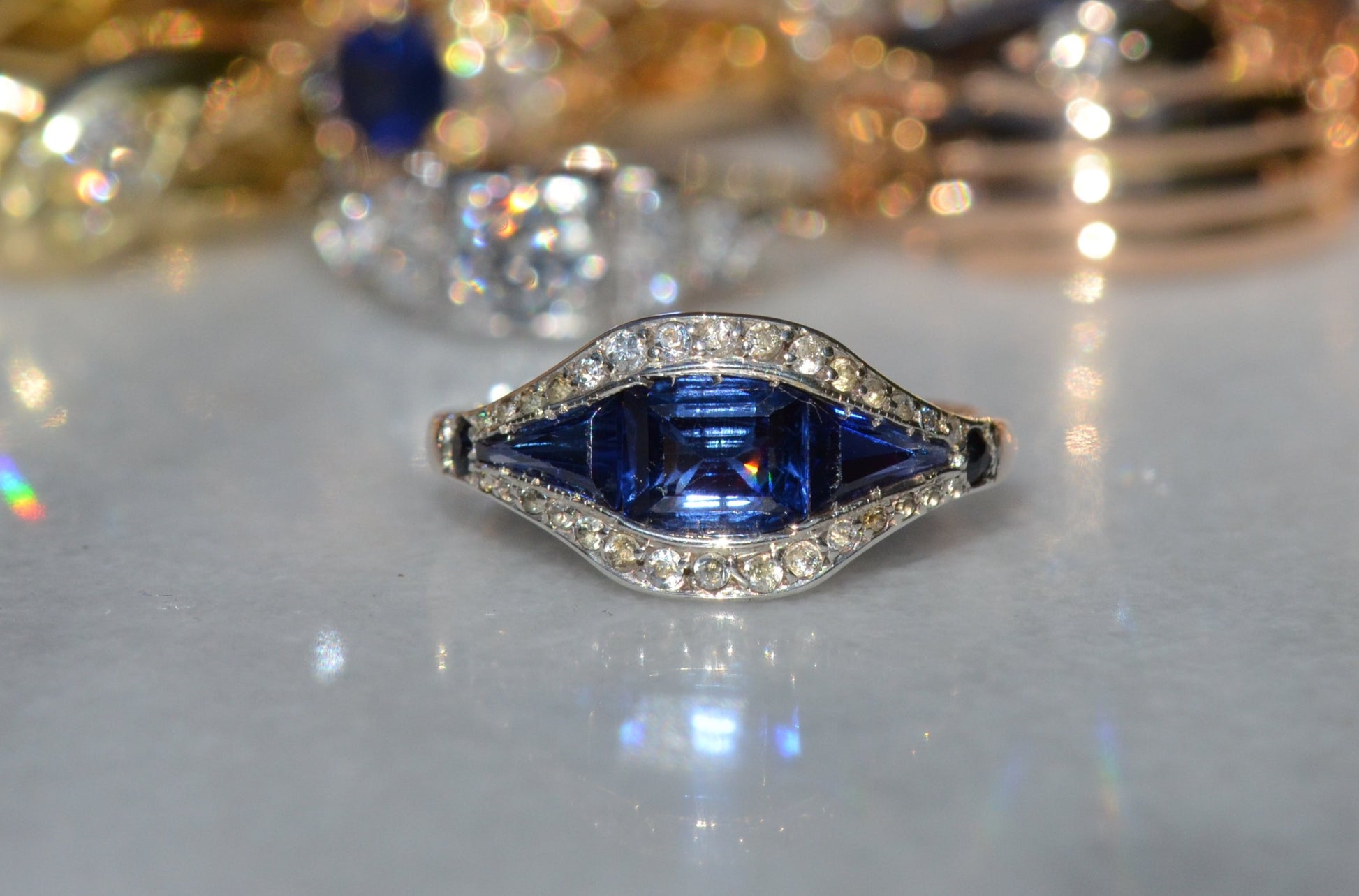 A closely cropped macro of an Art Deco ring, head on. The rich blue centre shows a flash of orange reflected from a back facet.