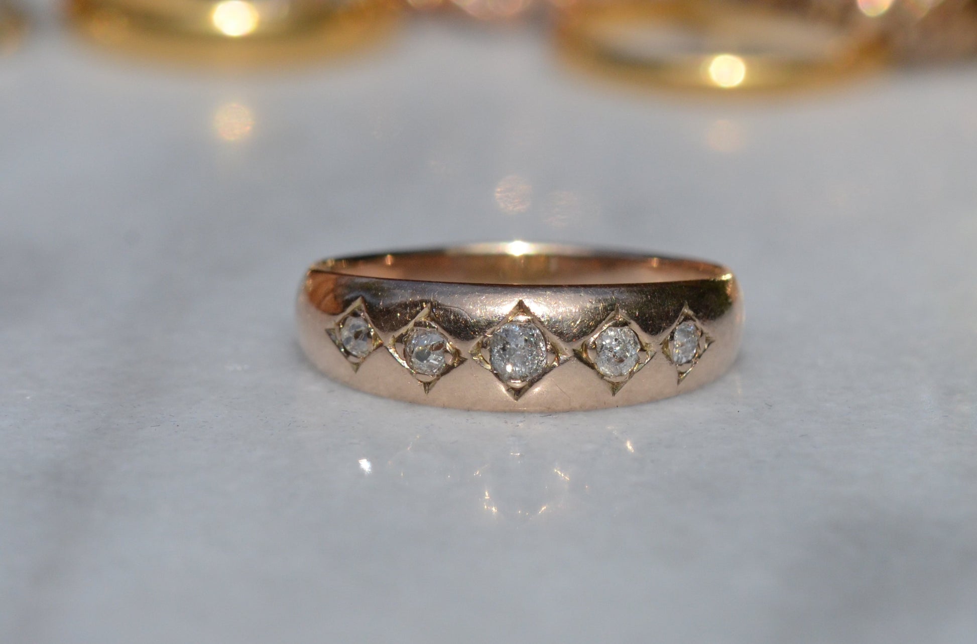 A tightly-cropped macro shot of the Victorian ring, showing the hand-cut diamond-shaped frames that hold each cushion-shaped stone. The old mine cut diamonds have internal fractures and inclusions but still sparkle in the direct sun, and the gold is weathered from a century of wear. The ring is facing head-on.