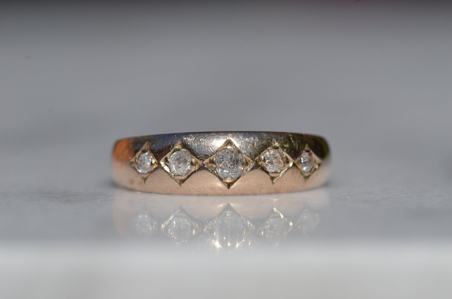 A tightly-cropped macro shot of the Victorian ring, showing the hand-cut diamond-shaped frames that hold each cushion-shaped stone. The old mine cut diamonds have internal fractures and inclusions but still sparkle in the direct sun, and the gold is weathered from a century of wear. The ring is facing head-on.