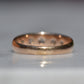 The ring shown from behind, with the back of the band in focus. The metal is scuffed and worn with a patina and subtle evidence of multiple past resizing over the years, seen in slight changes to the hue of the gold.
