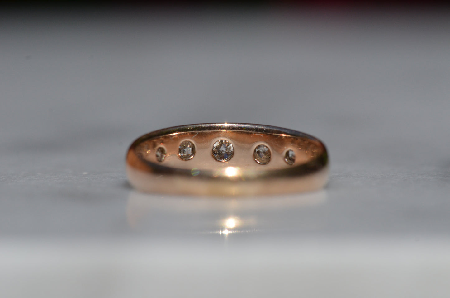 The ring is shown from behind, with the back of the mount in focus, showing the solid construction and smooth gold as well as the open backs behind each diamond setting.