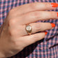 The ring is shown on the right ring finger of a Caucasian model in bright orangey-red nail polish.