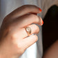 The ring is shown on the right ring finger of a Caucasian model in bright orangey-red nail polish.