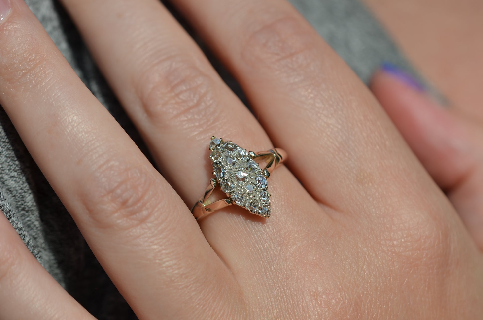 A closely cropped macro photo of the antique ring on a Caucasian model's left middle finger to show scale, photographed in natural light that dazzles on the diamonds.