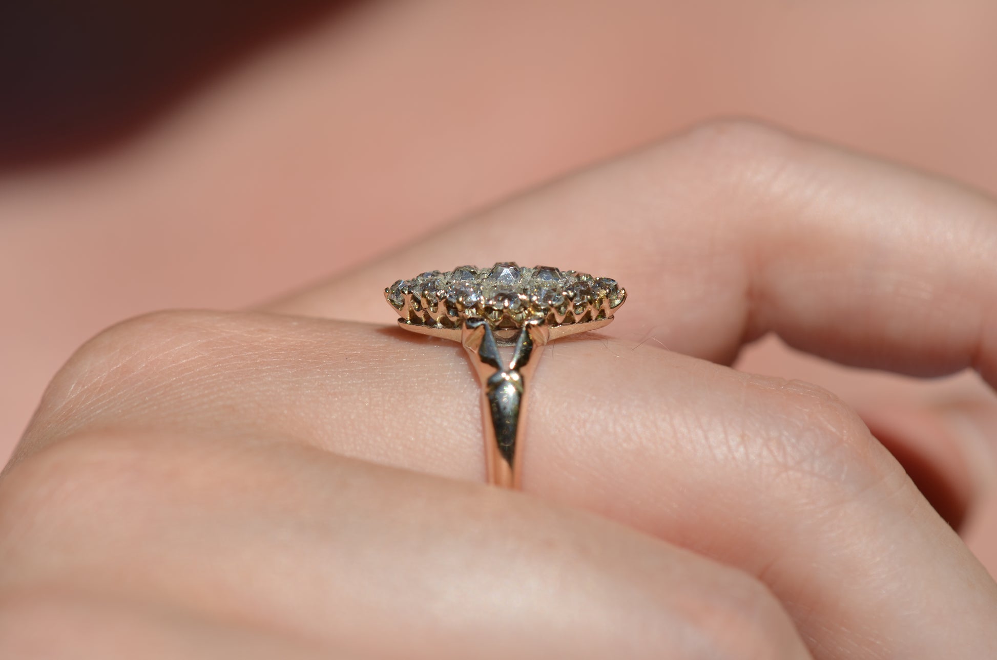 A closely cropped macro photo of the antique ring on a Caucasian model's right middle finger to show scale, photographed in natural light that dazzles on the diamonds. Shown in profile to highlight the low rise off the finger.