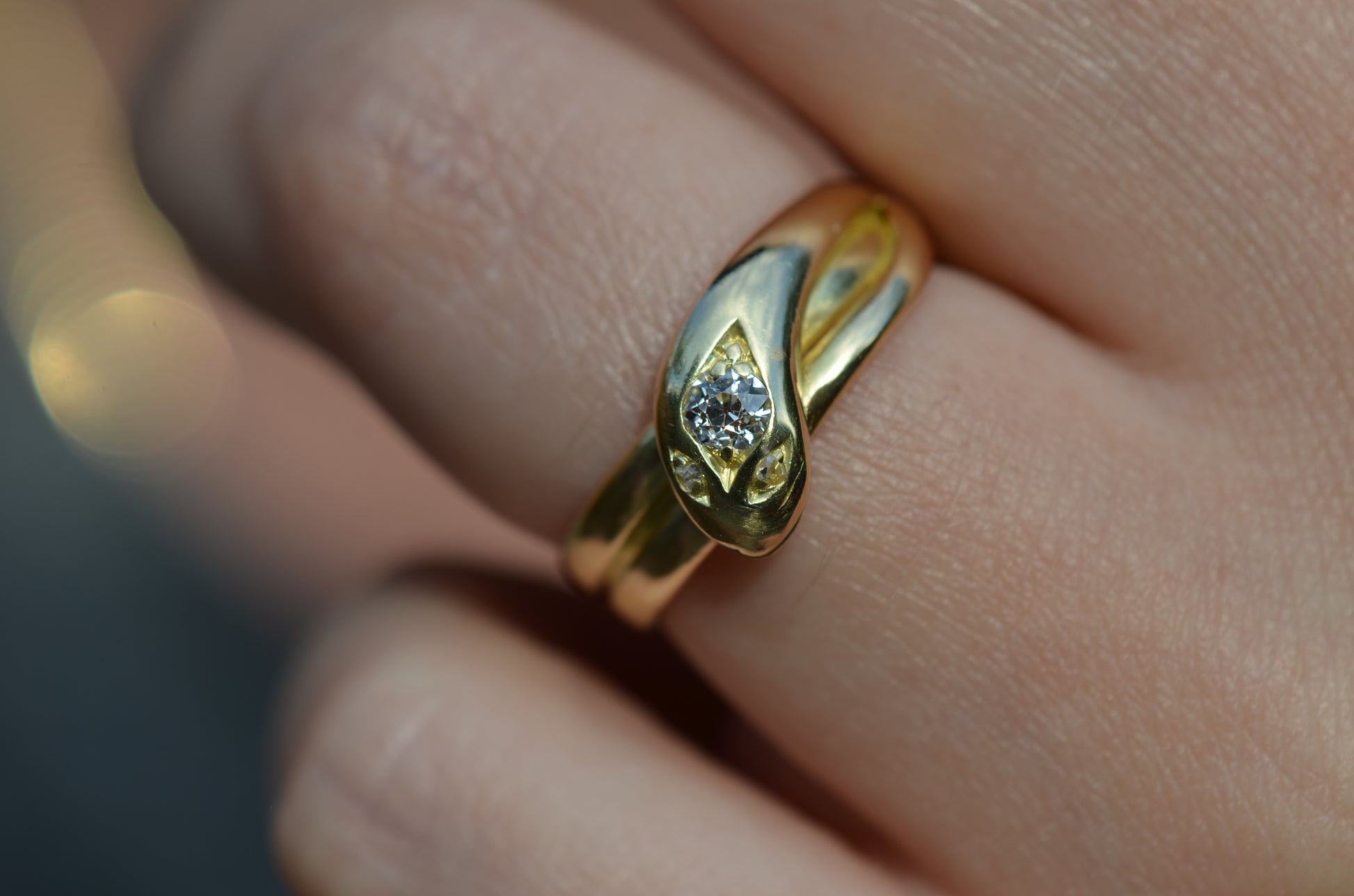 Macro of Victorian yellow gold snake ring with diamond head and eyes shown on the left ring finger of a Caucasian model to demonstrate scale while worn.