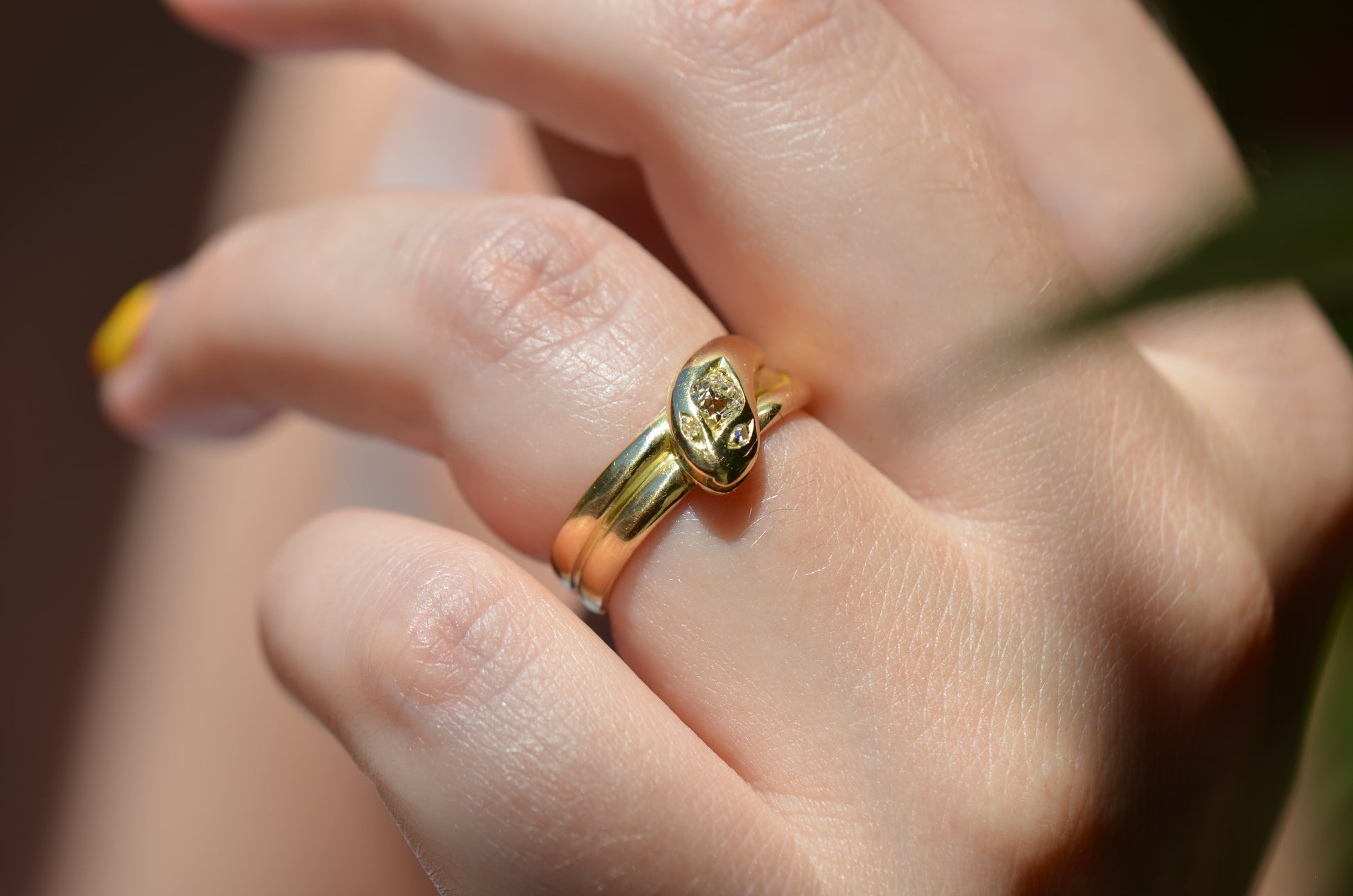 Medium-close view of Victorian yellow gold snake ring with diamond head and eyes shown on the left ring finger of a Caucasian model to demonstrate scale while worn.
