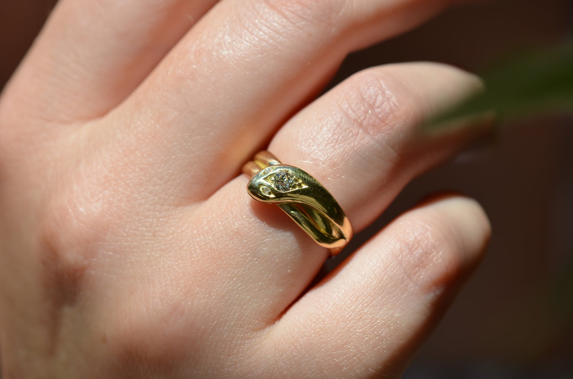 Macro of Victorian yellow gold snake ring with diamond head and eyes shown on the right ring finger of a Caucasian model to demonstrate scale while worn.