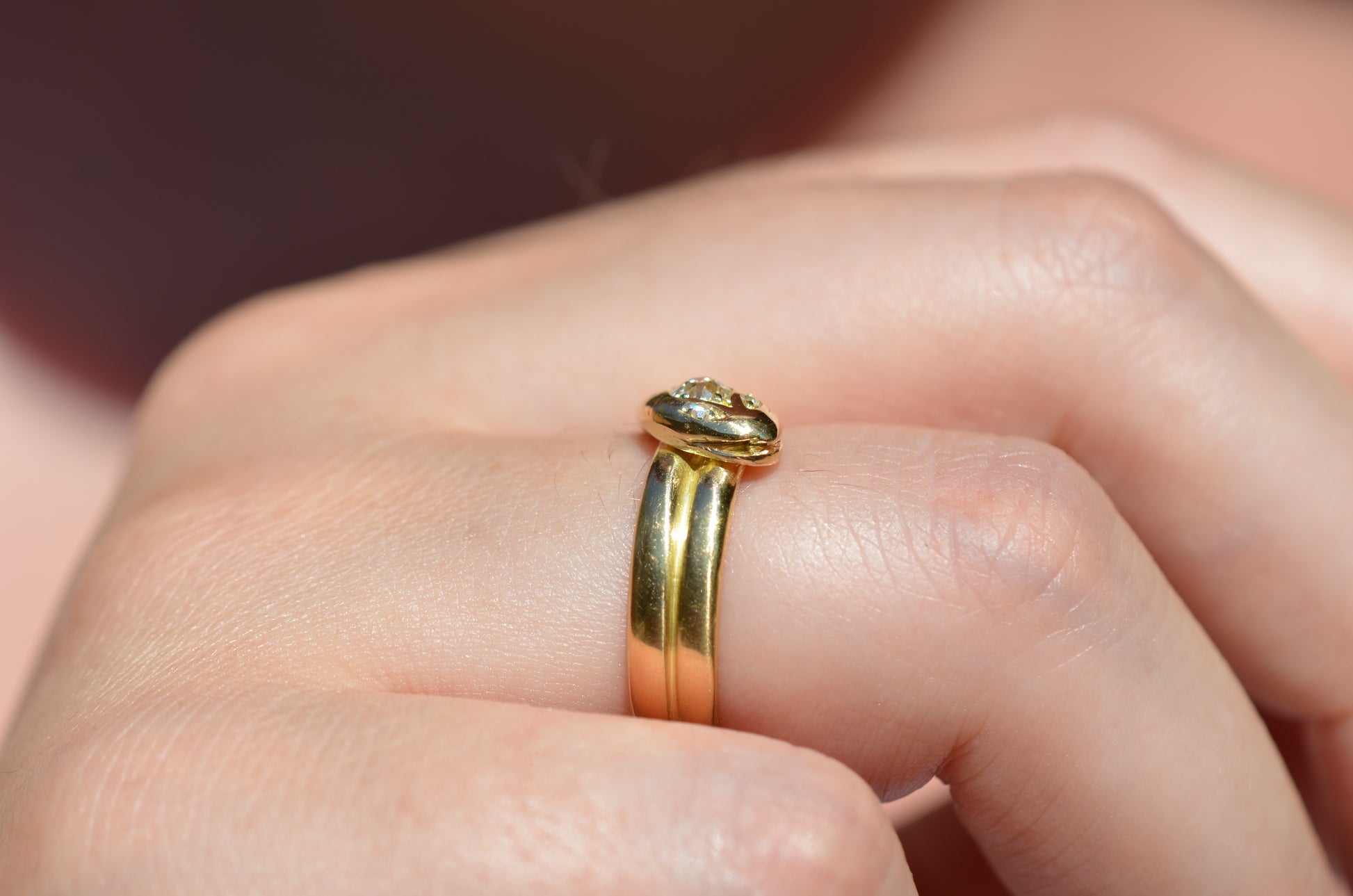 Macro of Victorian yellow gold snake ring with diamond head and eyes shown on the right ring finger of a Caucasian model to demonstrate scale while worn. View is from the side to highlight the snake's face and lightly open mouth, as well as the rise off the finger.