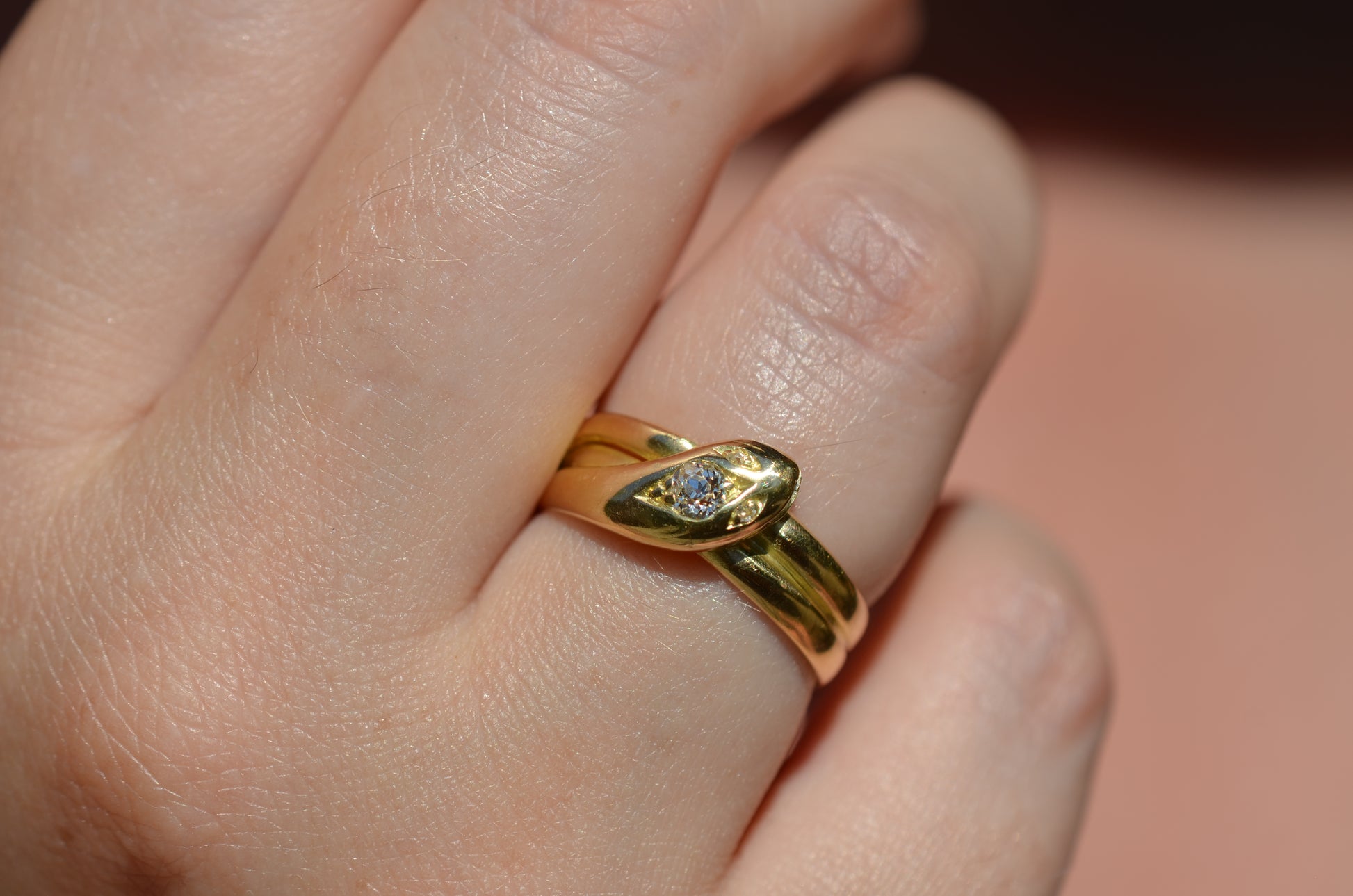 Macro of Victorian yellow gold snake ring with diamond head and eyes shown on the right ring finger of a Caucasian model to demonstrate scale while worn.