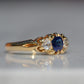 A Victorian ring in yellow gold with swirling shoulders and a central vivid blue sapphire flanked by a pair of old mine cut diamonds, photographed turned to the right to highlight the side view of the ring.