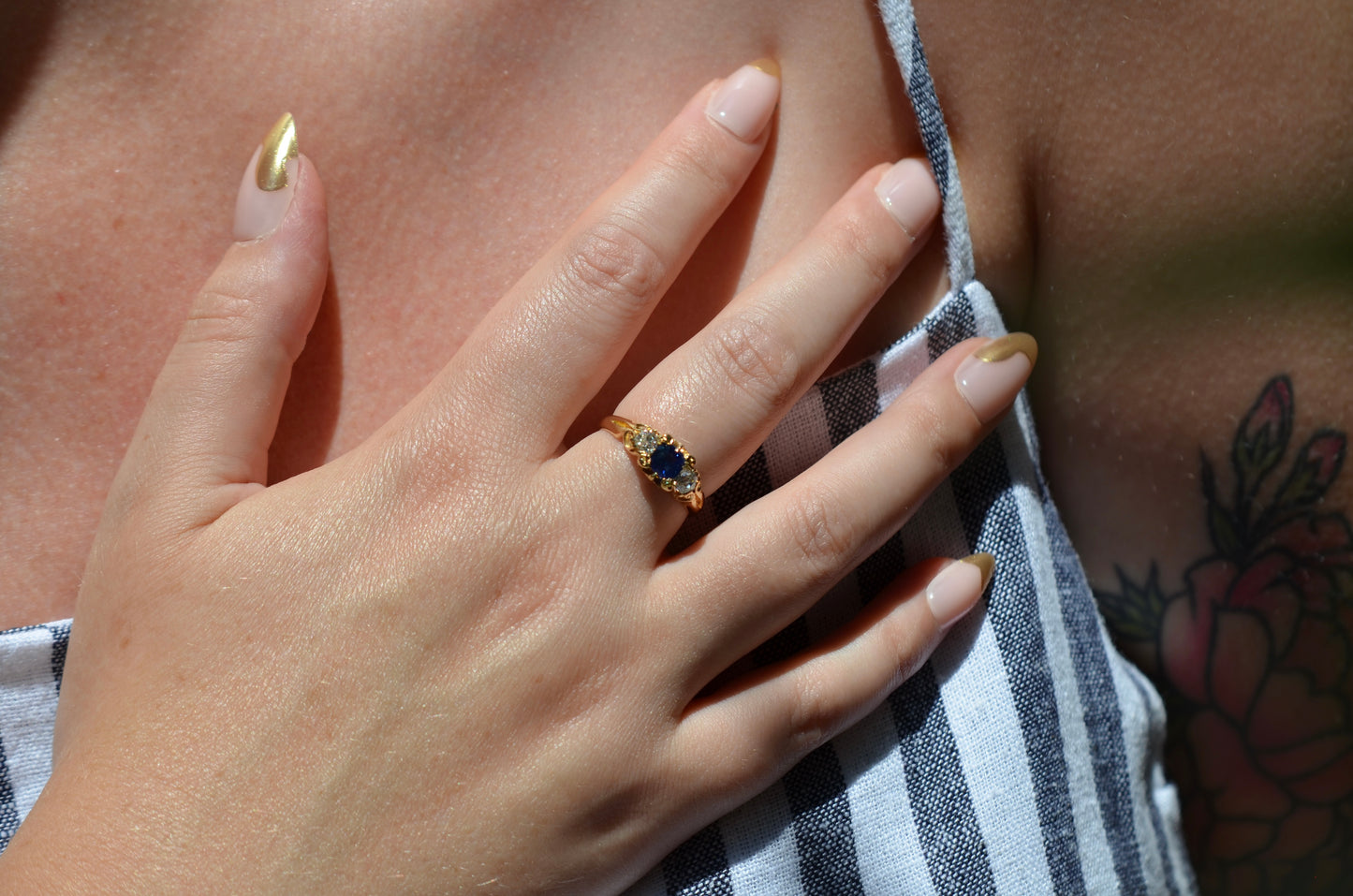 The antique sapphire and diamond trilogy ring, worn on the right middle finger of a hand resting across the model's chest at close-medium distance to show scale on the hand. Shown on a Caucasian model.