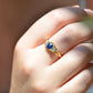 The antique sapphire and diamond trilogy ring, worn on the right middle finger of a hand in front of the model's chest at close-medium distance to show scale on the hand. Shown on a Caucasian model.