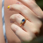 The antique sapphire and diamond trilogy ring, worn on the right middle finger of a hand in front of the model's chest at close-medium distance to show scale on the hand. Shown on a Caucasian model.