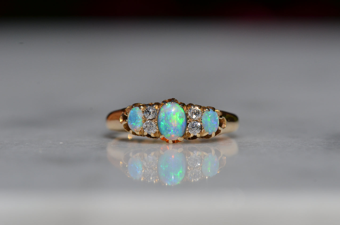 A closely-cropped macro of the Victorian ring, showcasing the strong green and blue play of color in the opals with a hint of violet and orange. The ring is photographed head-on.