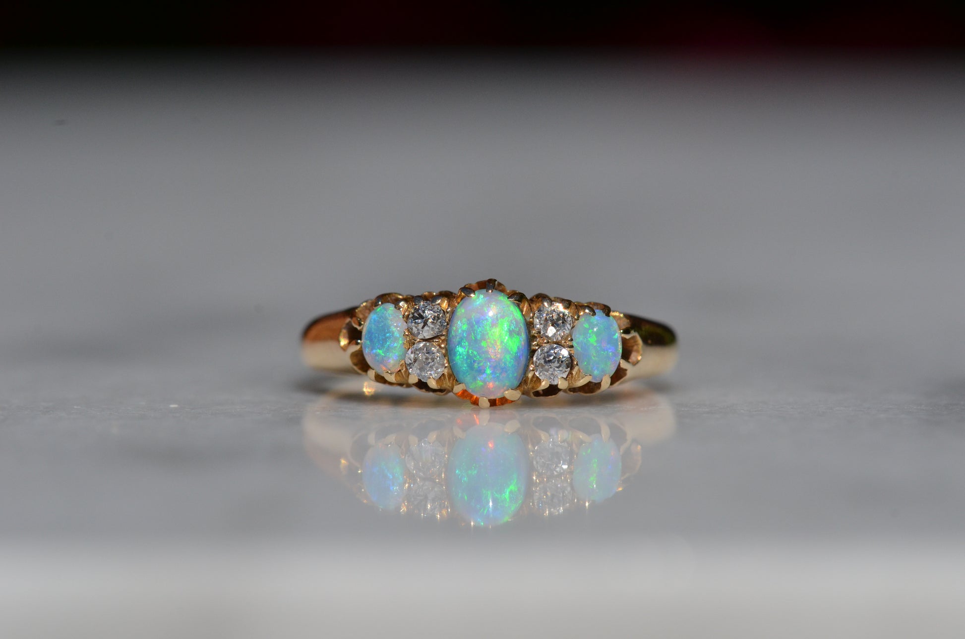 A closely-cropped macro of the Victorian ring, showcasing the strong green and blue play of color in the opals with a hint of violet and orange. The ring is photographed head-on.