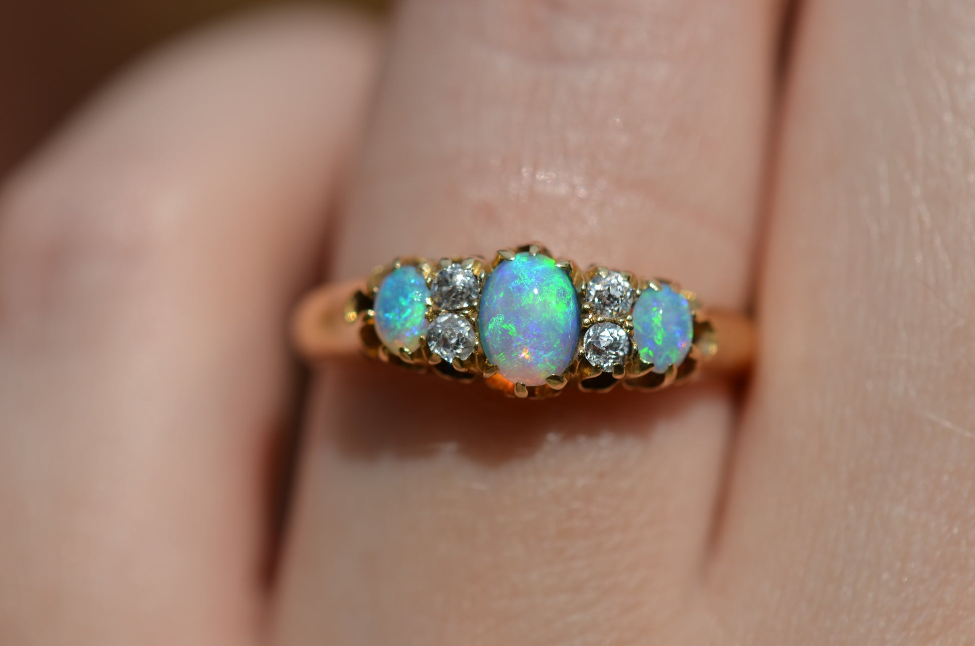 A very tightly cropped macro of the ring on a Caucasian model, showing the scale to the ring on the hand as well as the play of color of the opals in direct sunlight.