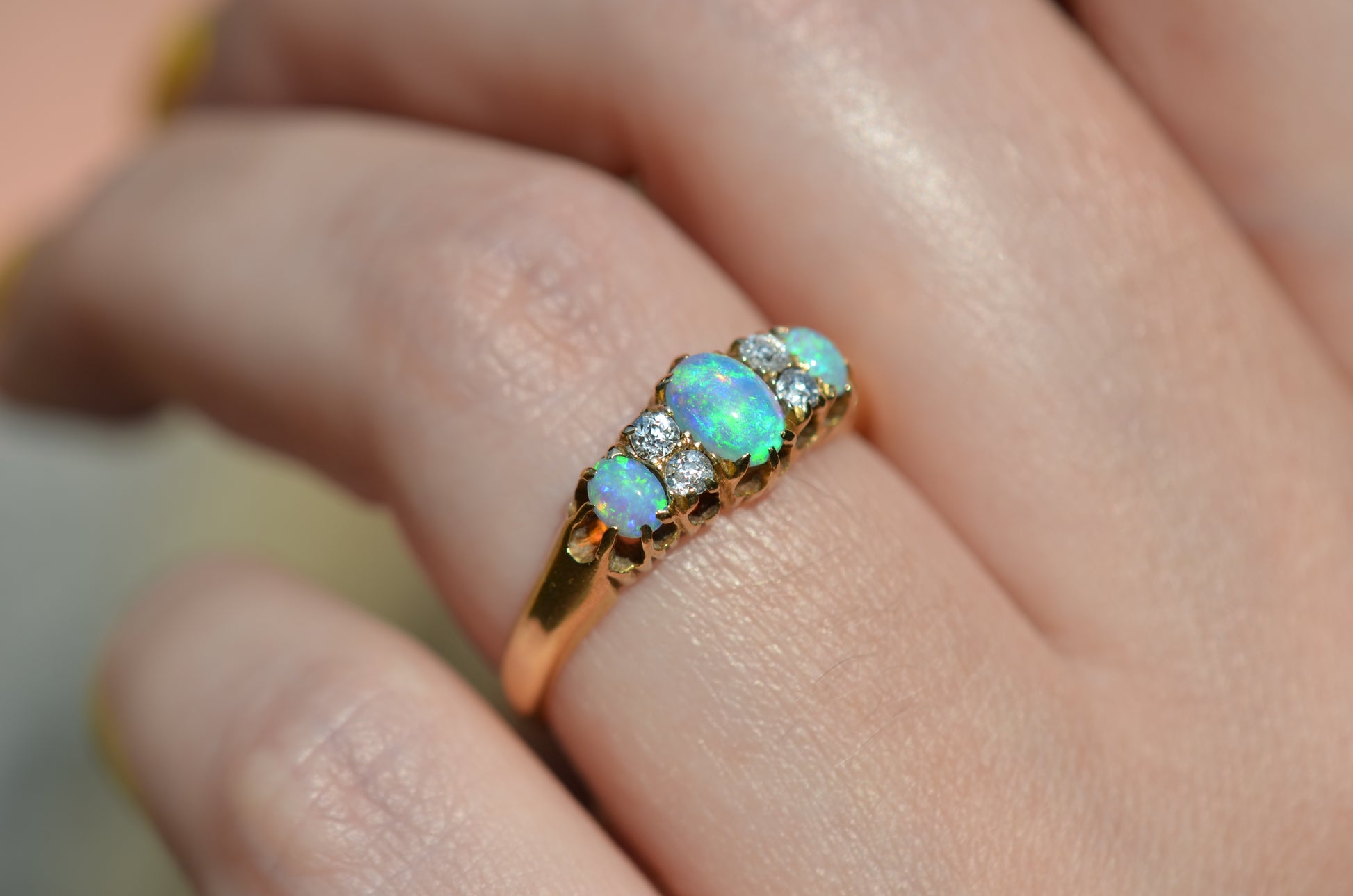 A very tightly cropped macro of the ring on a Caucasian model, showing the scale to the ring on the hand as well as the play of color of the opals in direct sunlight.