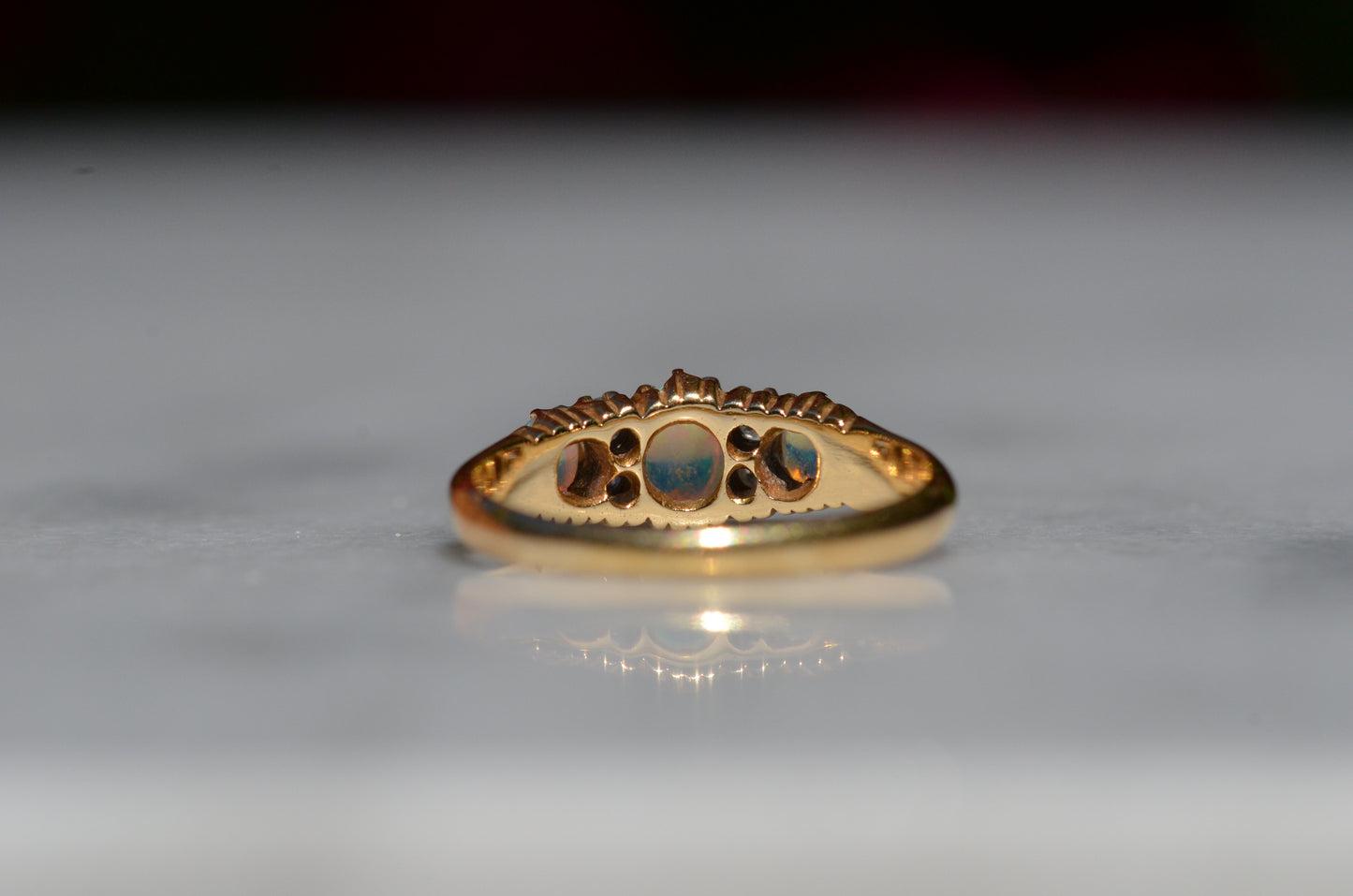 A closely-cropped macro of the Victorian ring, showcasing the strong green and blue play of color in the opals with a hint of violet and orange. The ring is photographed from behind, focused on the back of the setting and underside of the stones.