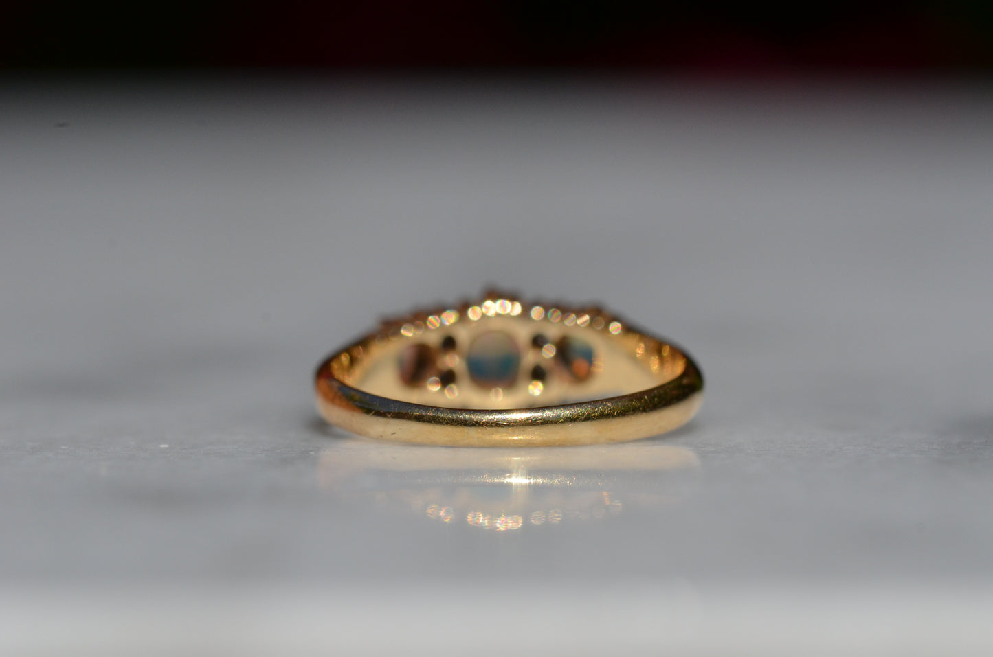 A closely-cropped macro of the Victorian ring, showcasing the strong green and blue play of color in the opals with a hint of violet and orange. The ring is photographed from the back, focused on the smooth deep yellow gold band.