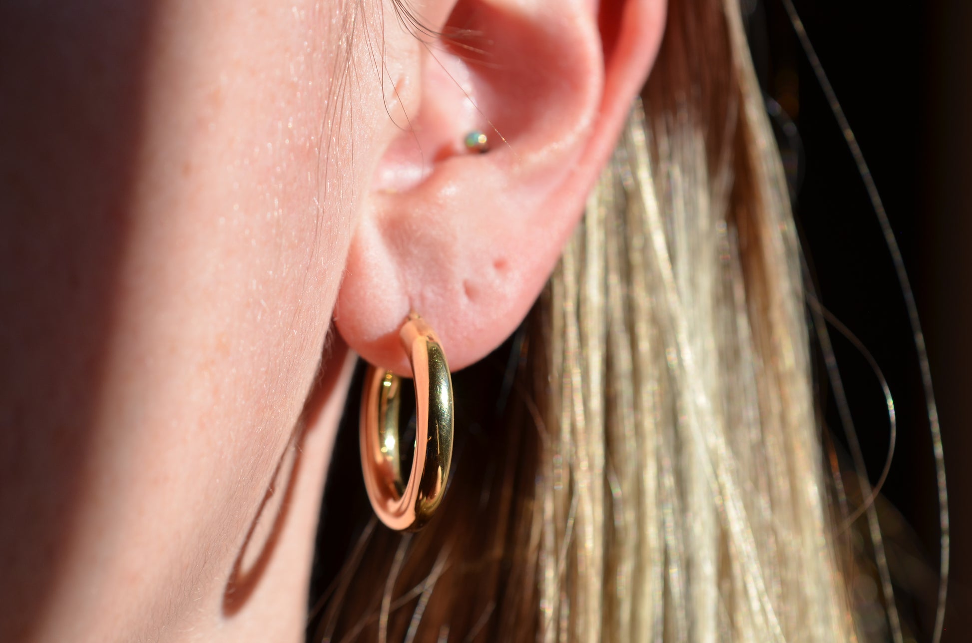 in direct sunlight, the hoop earrings are shown on a caucasian model's first piercing to show scale. the fit is loose.