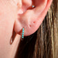 in direct sunlight, a single of the hoops is shown on the first lobe piercing of a caucasian model. the fit is moderately snug but not tight to the lobe.