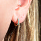 in direct sunlight, a single of the hoops is shown on the first lobe piercing of a caucasian model. the fit is moderately snug but not tight to the lobe.