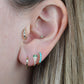a caucasian model wears the featured earring in a third lobe piercing, where the fit is snug. additionally visible are a gold and baguette diamond small hoop in the first piercing, a pavé diamond and emerald-eyed snake small hoop in the second piercing, a multi-stone baguette diamond hoop in the tragus piercing, and a small opal stud in the conch piercing.