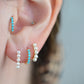 a caucasian model wears the featured turquoise small hoop in both the second lobe piercing and tragus piercing. in the first and third lobe piercing are a pair of gold and pearl small hoop earrings.