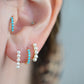 a caucasian model wears the featured turquoise small hoop in both the second lobe piercing and tragus piercing. in the first and third lobe piercing are a pair of gold and pearl small hoop earrings.