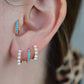 a caucasian model wears the featured turquoise small hoop in both the second lobe piercing and tragus piercing. in the first and third lobe piercing are a pair of gold and pearl small hoop earrings.