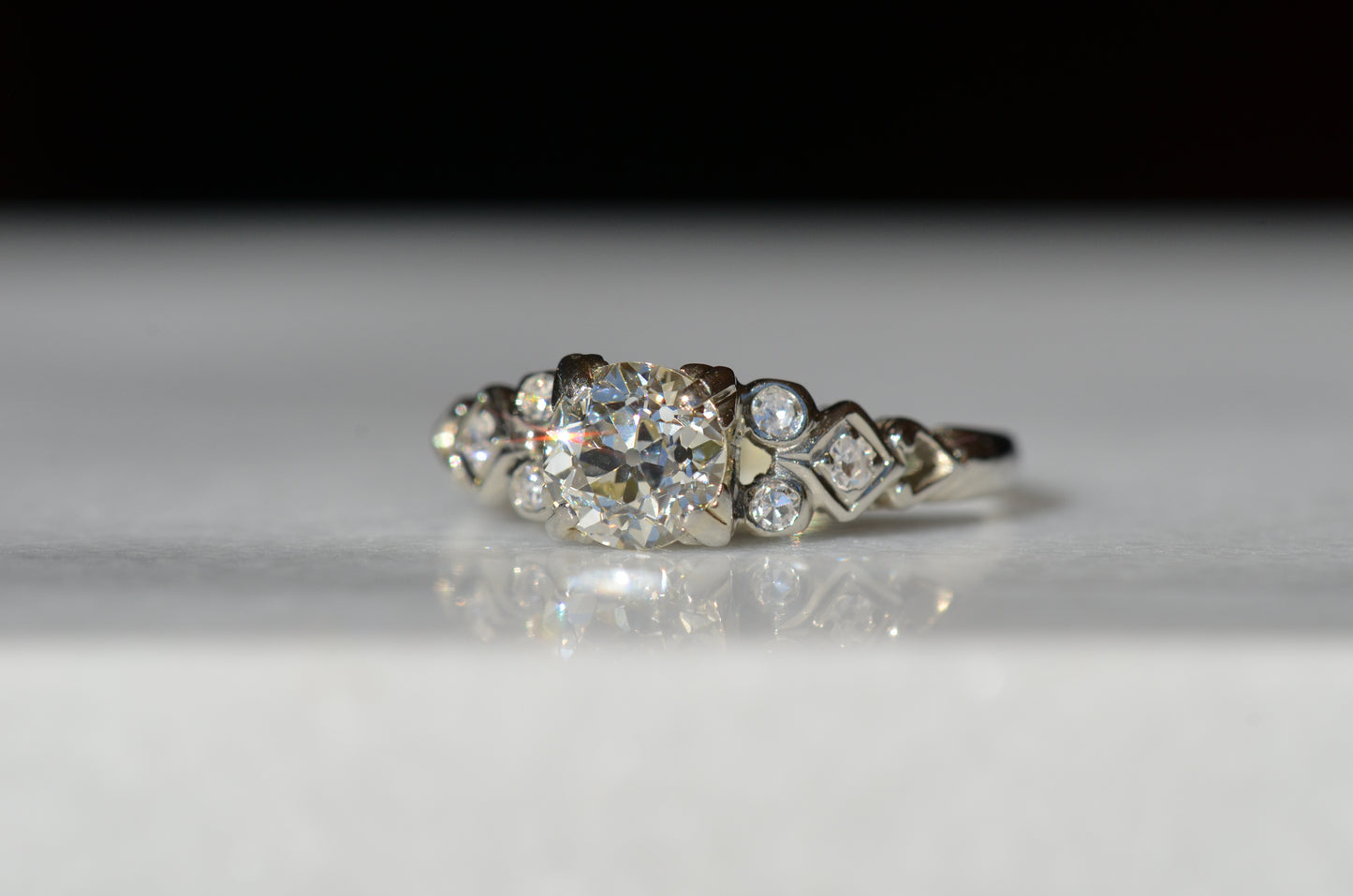 ring in direct sunlight, angled slightly askew. a flash of orangey-red light radiates off the central diamond, and one shoulder is also in focus.