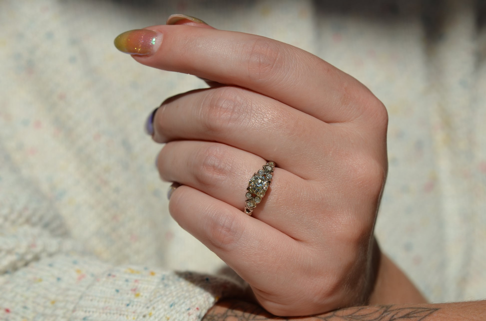 the ring style on a caucasian model, worn on the left ring finger. in direct sunlight, the primary diamond shows moderate warm (yellow) undertones.