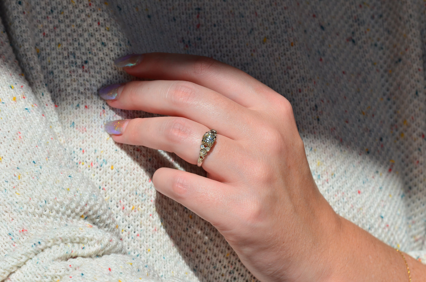 the ring is styled on a caucasian model's left ring finger, with the hand held casually to the chest. 