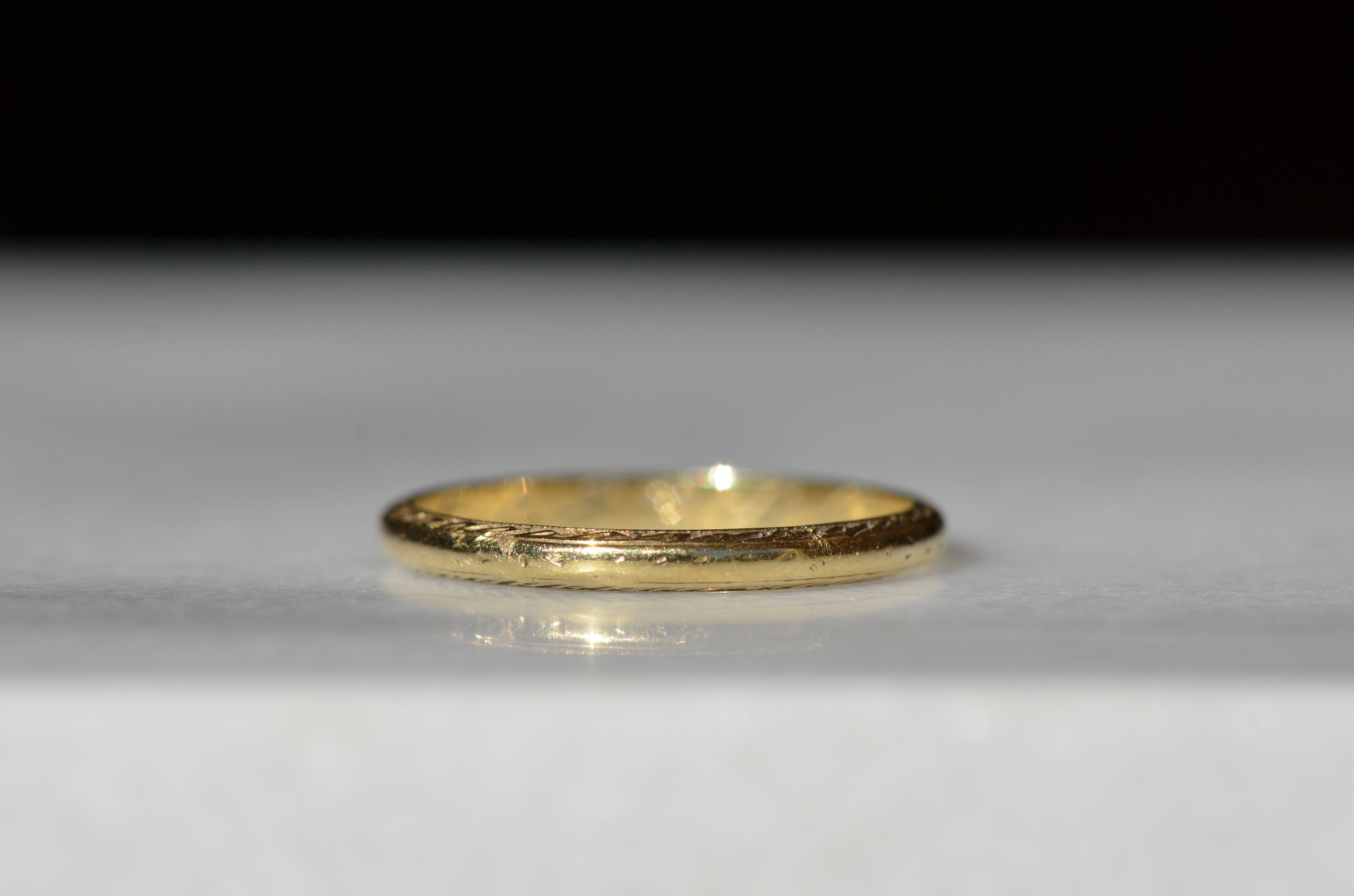ring shown in direct sunlight on a pale grey marble background. the engraved pattern has been worn away on the outer surface of the ring, leaving only the faintest remnants. 