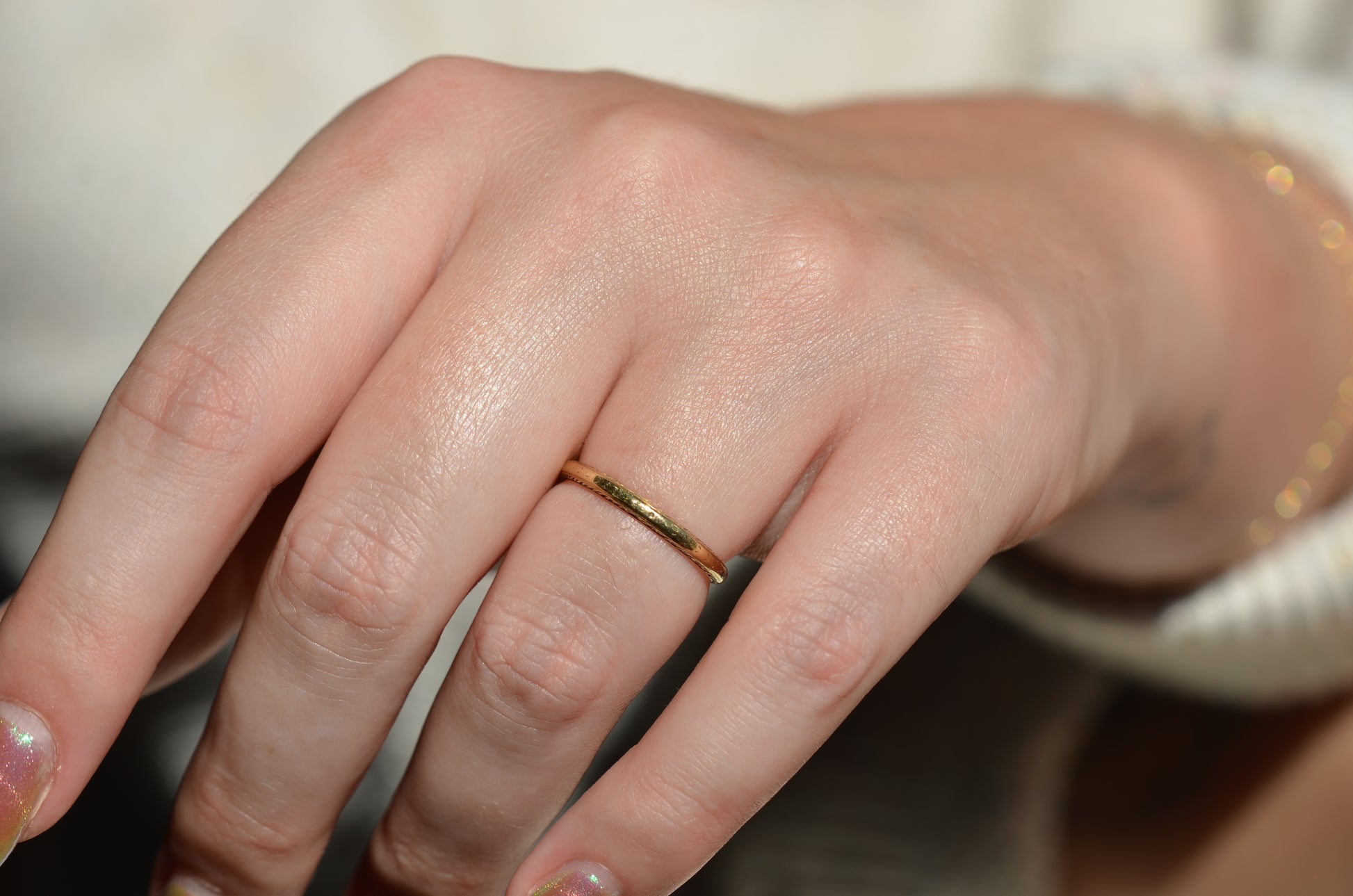 ring shown on the left ring finger of a caucasian model, shown in direct sunlight. image shows full hand and some body in order to help provide a sense of scale of the slim ring on the hand.